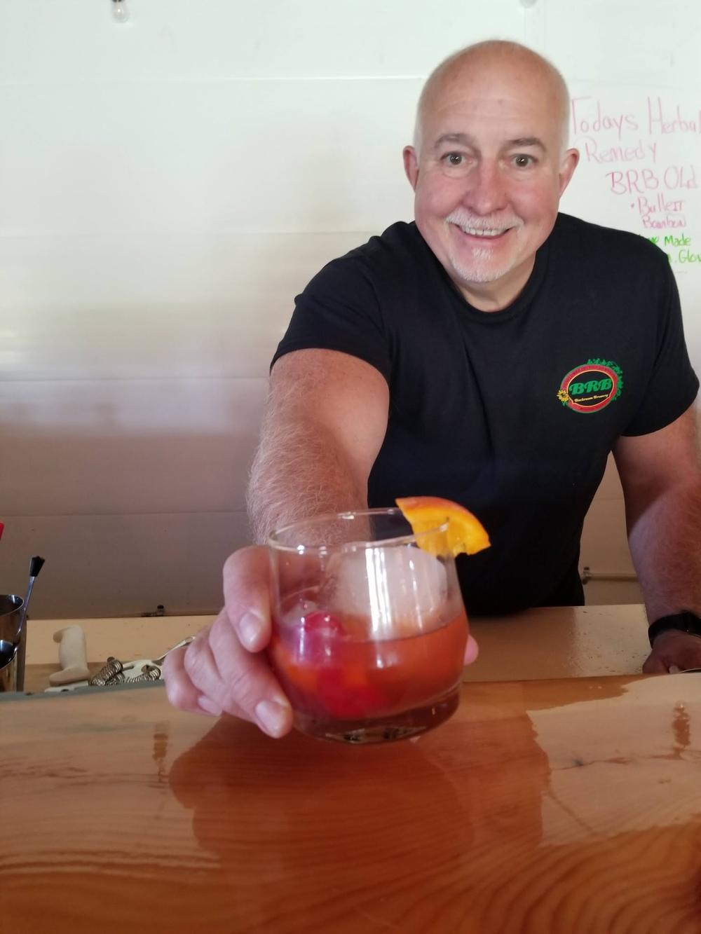 A bartender handing an old fashioned across the live-edge bar