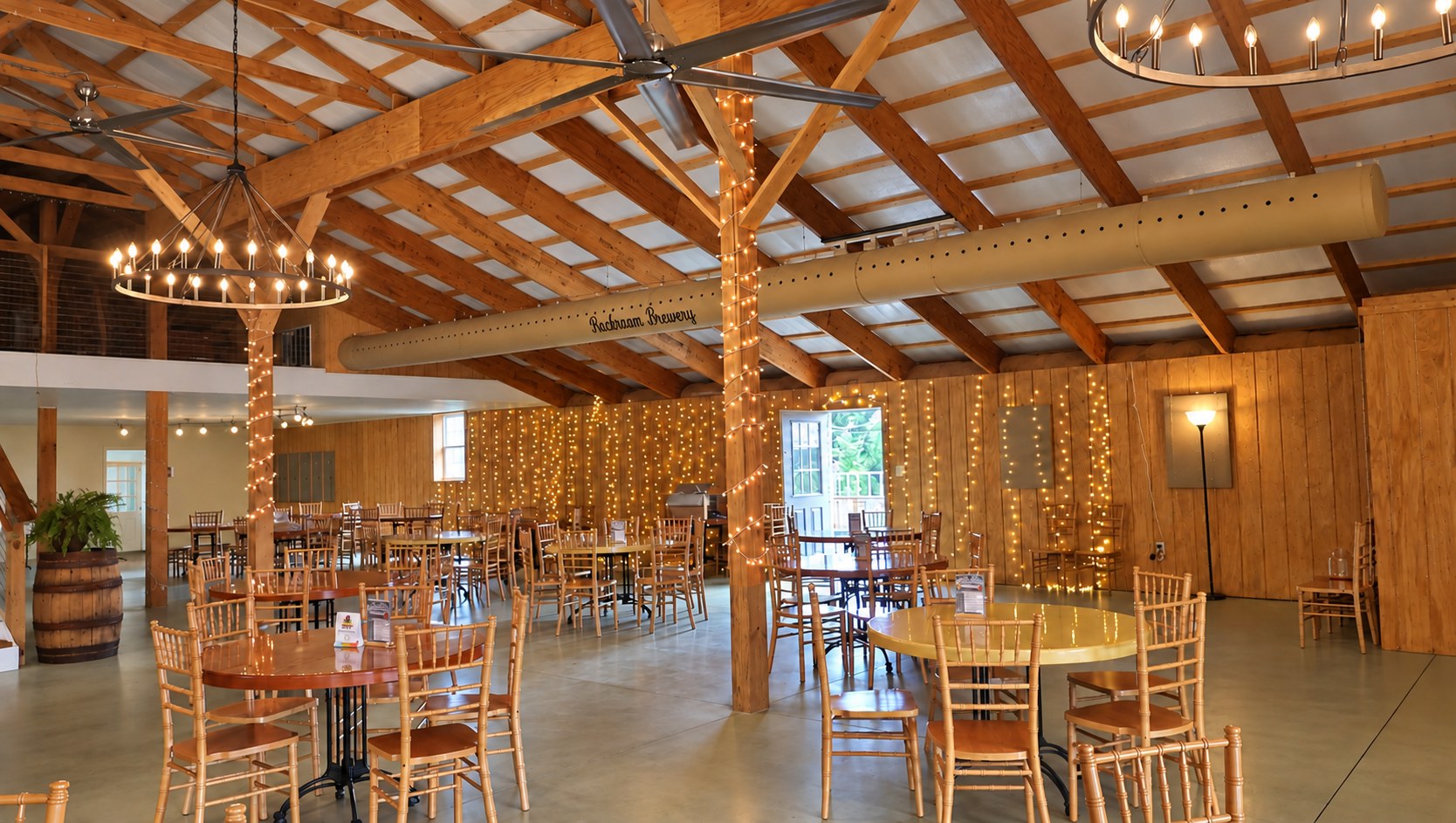 Wagon-wheel chandeliers and string lights over round tables in the Big Barn