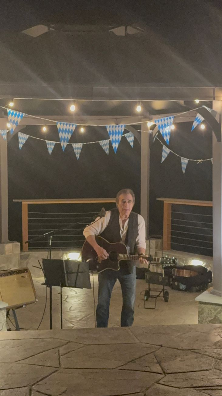 A guitarist playing at the gazebo at night under string lights and blue-and-white bunting