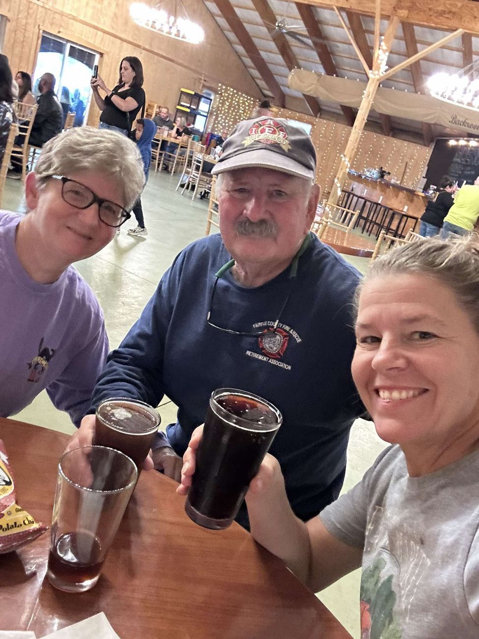Three guests at a table in the barn raising pint glasses toward the camera