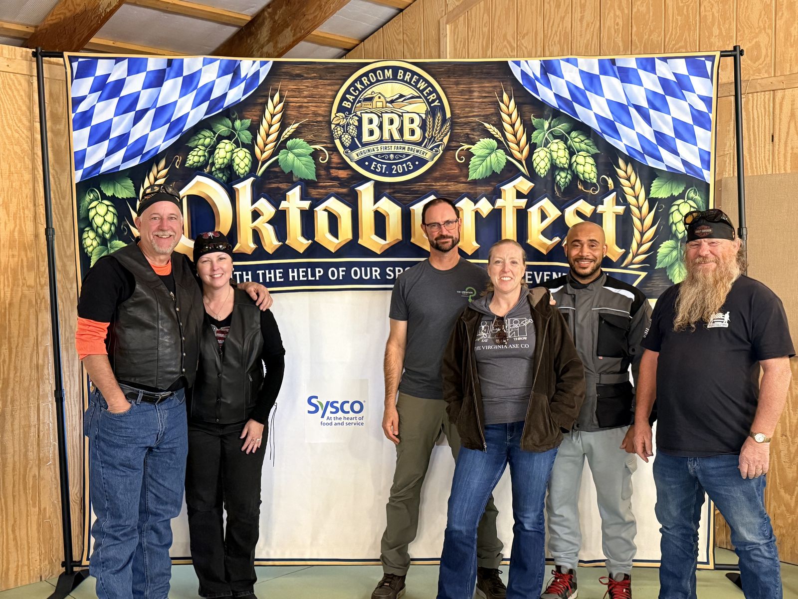 Six guests, several in riding vests and bandanas, standing in front of the Backroom Brewery Oktoberfest backdrop