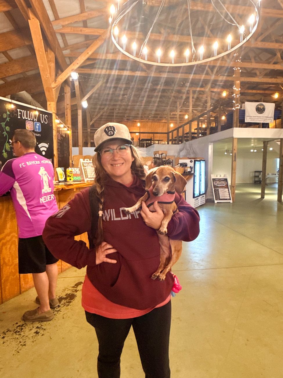 A guest holding a dachshund in a pink sweater beneath the barn chandelier